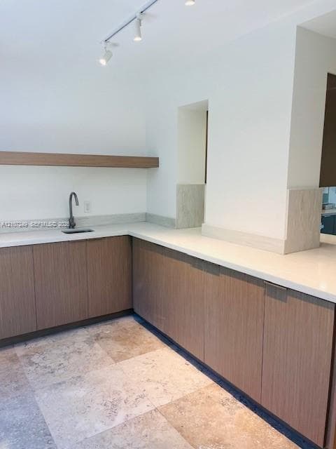 Modern kitchen featuring warm wood-finish cabinetry, sleek quartz countertops, contemporary track lighting, and a polished concrete flooring base with natural stone accents