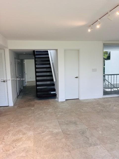 Interior space featuring large-format natural stone tile flooring, a staircase with dark-finished wood treads, adjustable track lighting, and a glass-paneled door