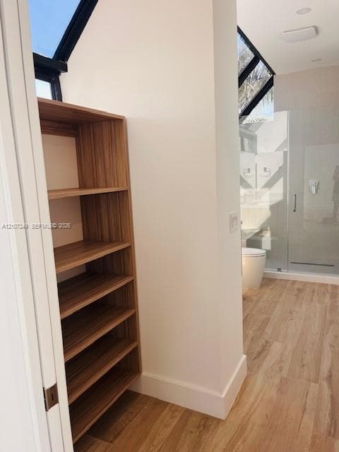 Built-in wood-finish shelving, sloped ceiling featuring a fixed skylight, wood-finish flooring, and glass-enclosed shower with chrome fixtures