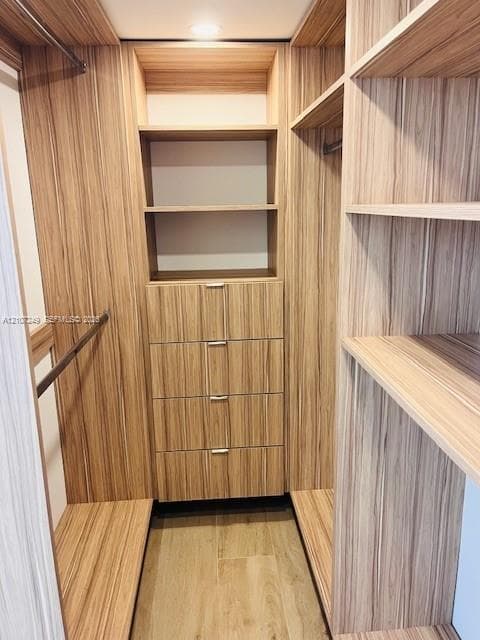 Custom walk-in closet featuring wood-finish cabinetry, built-in shelving, integrated dresser drawers with metal hardware, and dual hanging rods