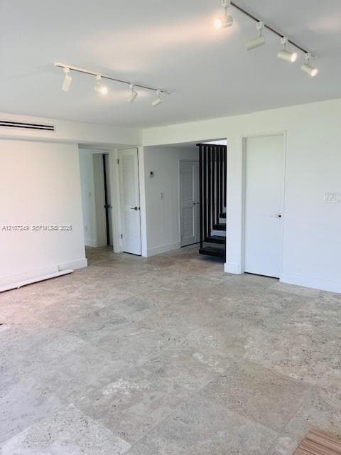 Open interior featuring large-format stone tile flooring, adjustable multi-head track lighting, solid-core interior doors, and custom vertical slat staircase railing