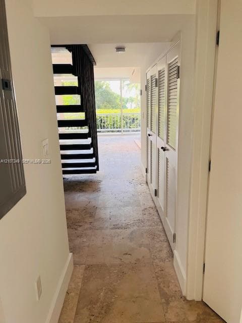 Interior hallway featuring natural stone flooring, white louvered closet doors, and an open-riser metal staircase