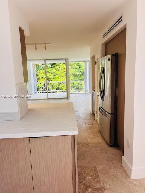 Kitchen featuring wood-finish cabinetry, stone-style countertops, stainless steel appliances, stone flooring, and floor-to-ceiling glass sliding doors