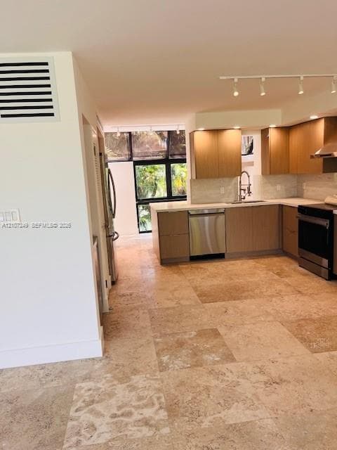 Kitchen featuring light-finish wood cabinetry, stainless steel appliances, white stone countertops, stone tile flooring, and track lighting