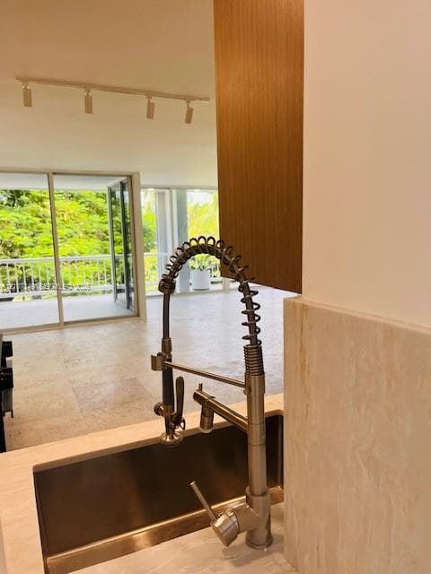 Kitchen featuring a stainless steel undermount sink, commercial-style pull-down faucet, stone-surround backsplash, wood-finish cabinetry, and track lighting