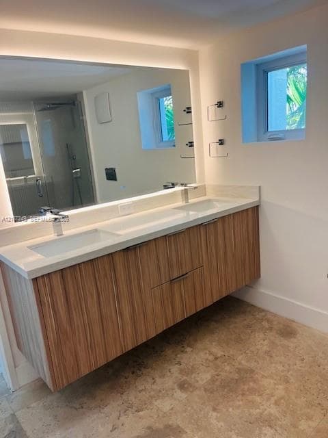 Floating wood-veneer vanity with dual integrated rectangular sinks, solid surface countertop, large wall-mounted mirror with integrated backlighting, and stone-tile flooring