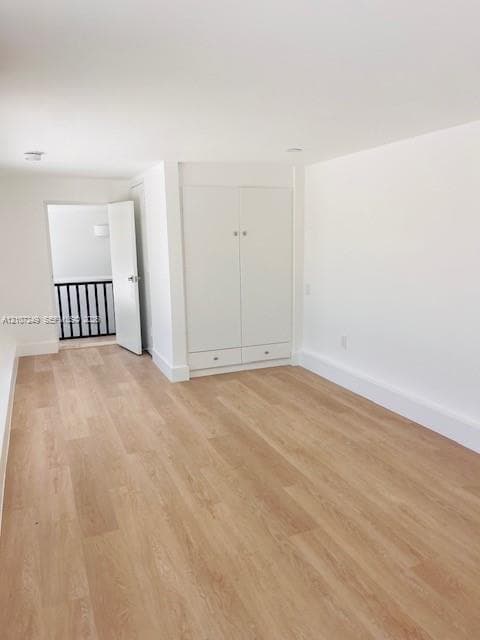 Room featuring light-toned wood-finish flooring, built-in floor-to-ceiling storage cabinetry with lower drawers, and a doorway revealing a metal balustrade