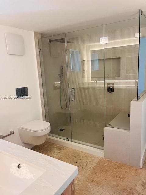 Walk-in glass-enclosed shower featuring a rainfall showerhead, handheld fixture, and built-in bench, wall-mounted toilet, and natural stone flooring
