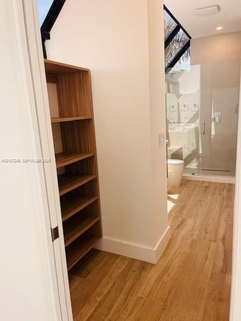 Built-in wood-finish shelving, wood-finish flooring, glass-enclosed shower, and sloped ceiling with clerestory window