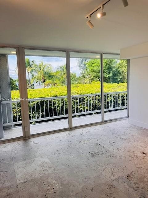Floor-to-ceiling glass sliding doors, stone tile flooring, adjustable track lighting, and a private balcony with metal railings