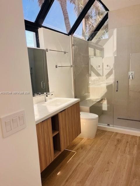 Bathroom featuring an angular skylight, wood-finish cabinetry, wood-finish flooring, a wall-mounted floating vanity with a stone countertop, and a walk-in shower with a glass enclosure