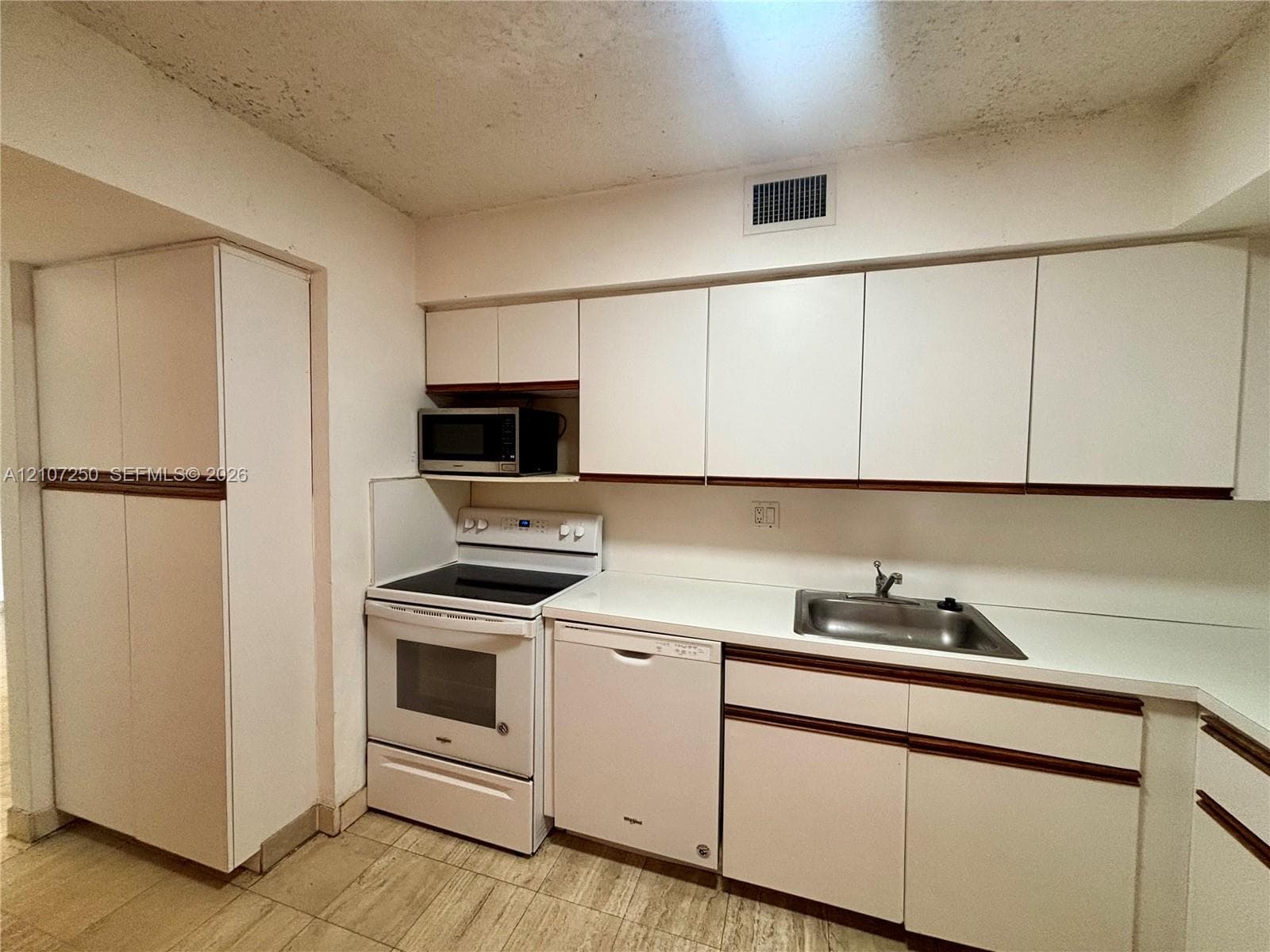 Kitchen featuring white cabinetry with integrated hardware, solid surface countertops, a stainless steel sink, and tile flooring