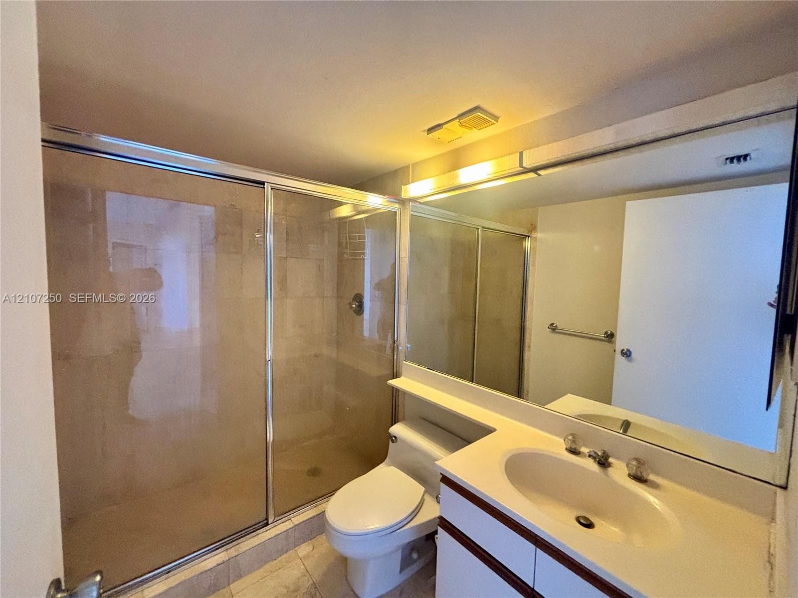 Full-width vanity with an integrated sink and countertop, large wall-mounted mirror, walk-in shower with glass sliding doors, and tiled flooring