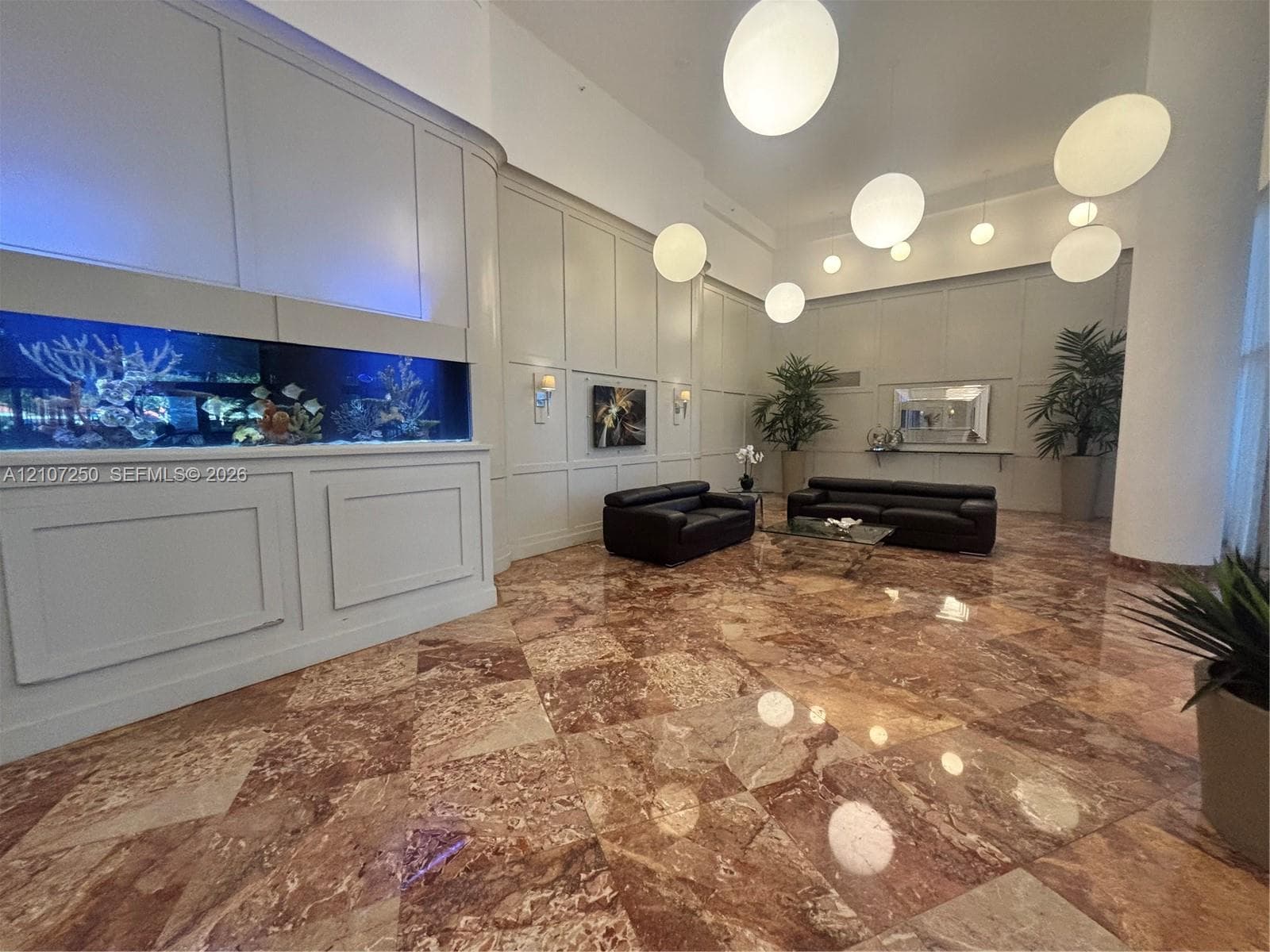 Grand lobby featuring polished stone tile flooring, floor-to-ceiling paneling, high ceilings, a built-in integrated aquarium, and globe pendant lighting