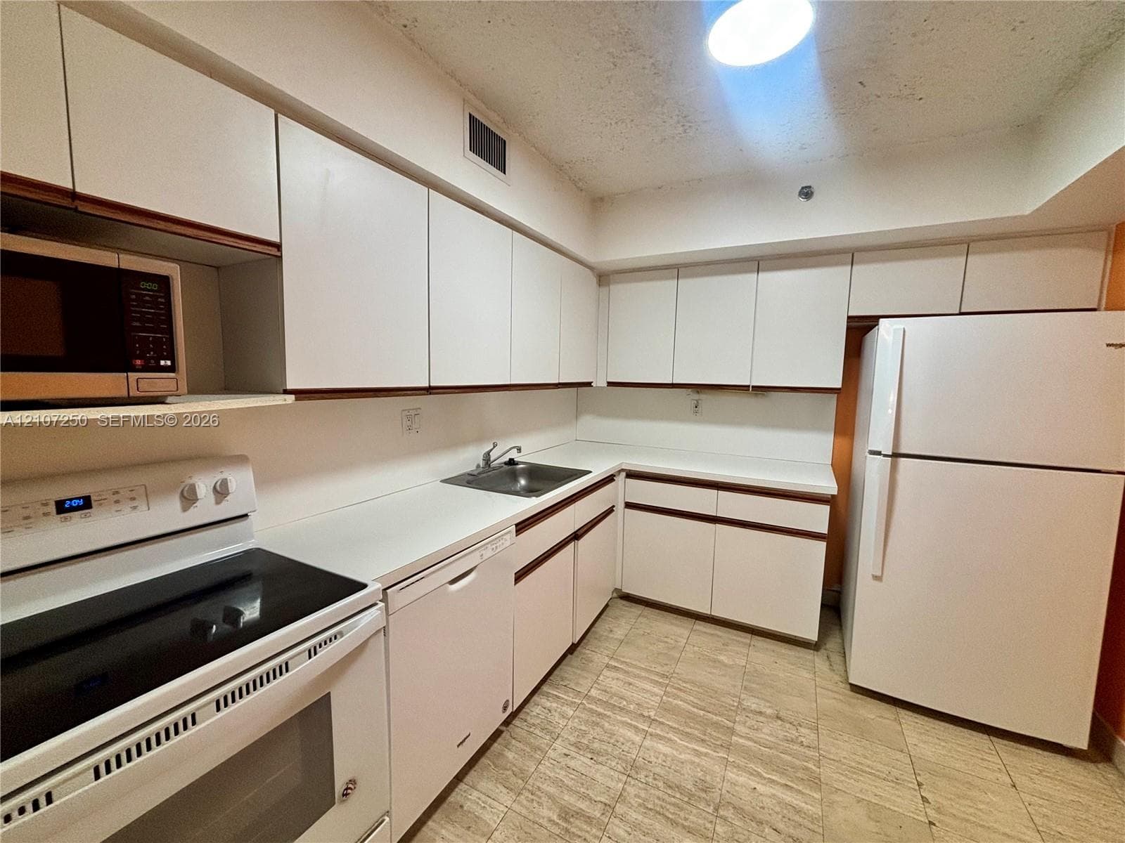 Kitchen featuring white cabinetry with dark trim, solid surface countertops, a stainless steel sink, tiled flooring, and white appliances
