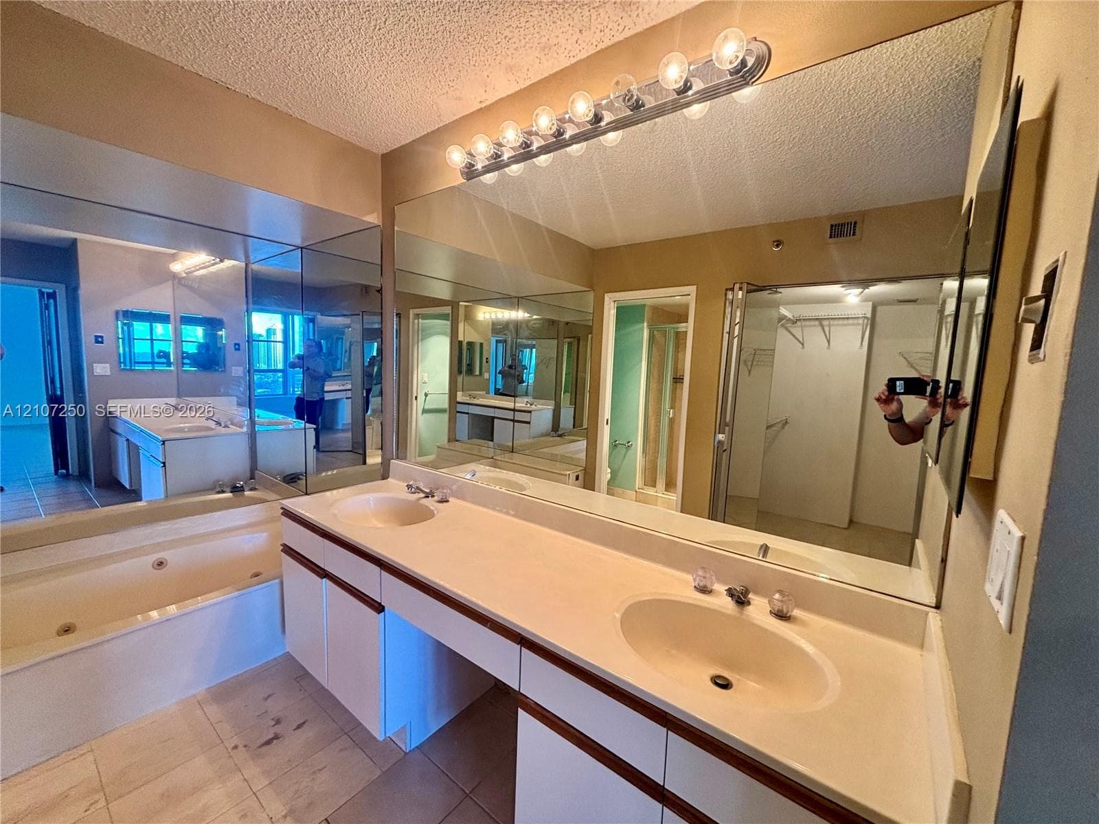 Dual-basin vanity with an integrated countertop, large-scale wall mirrors, jetted soaking tub, and linear vanity lighting