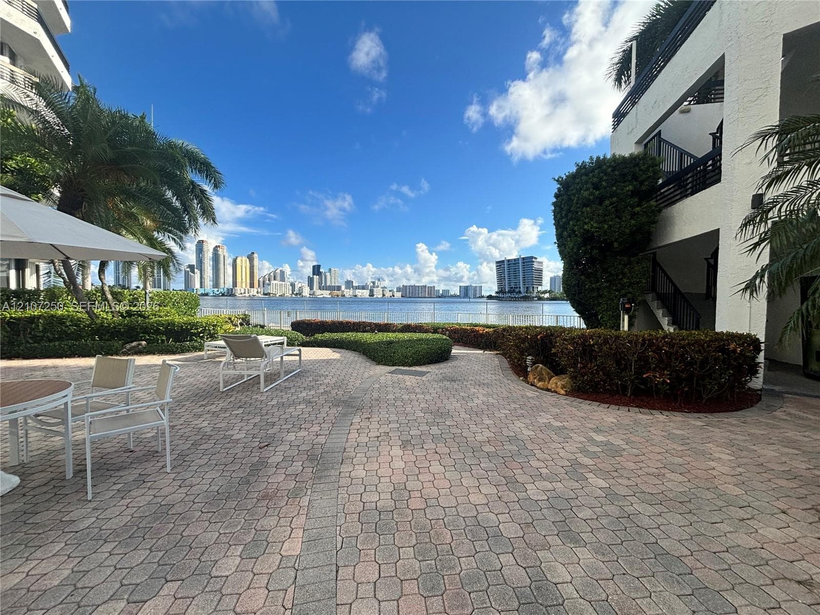 Paver patio featuring manicured hedging, established palm trees, and waterfront exposure