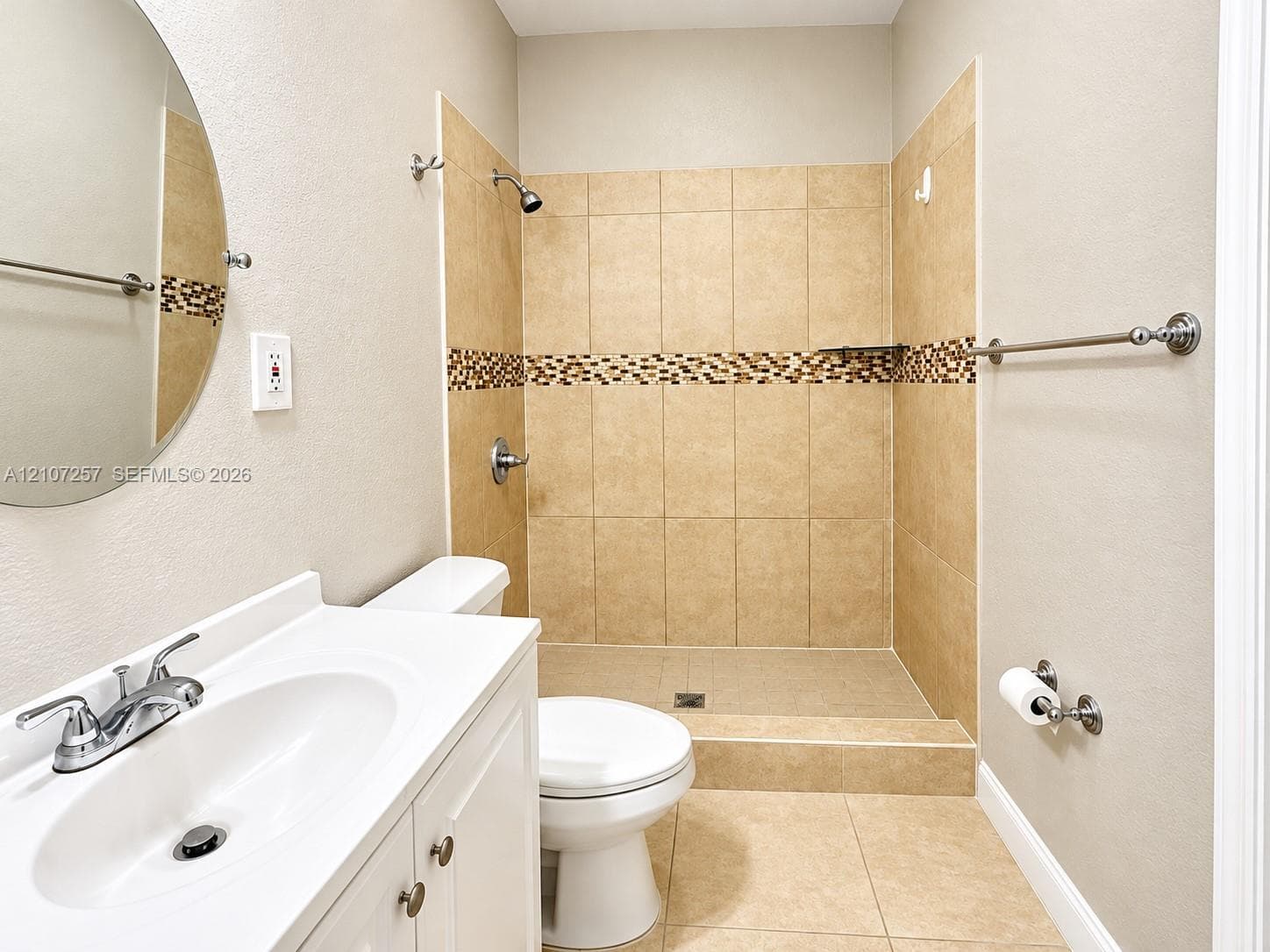Bathroom featuring a walk-in shower with neutral tile surround, decorative mosaic accent tile, and a crisp white vanity with integrated basin and polished chrome fixtures