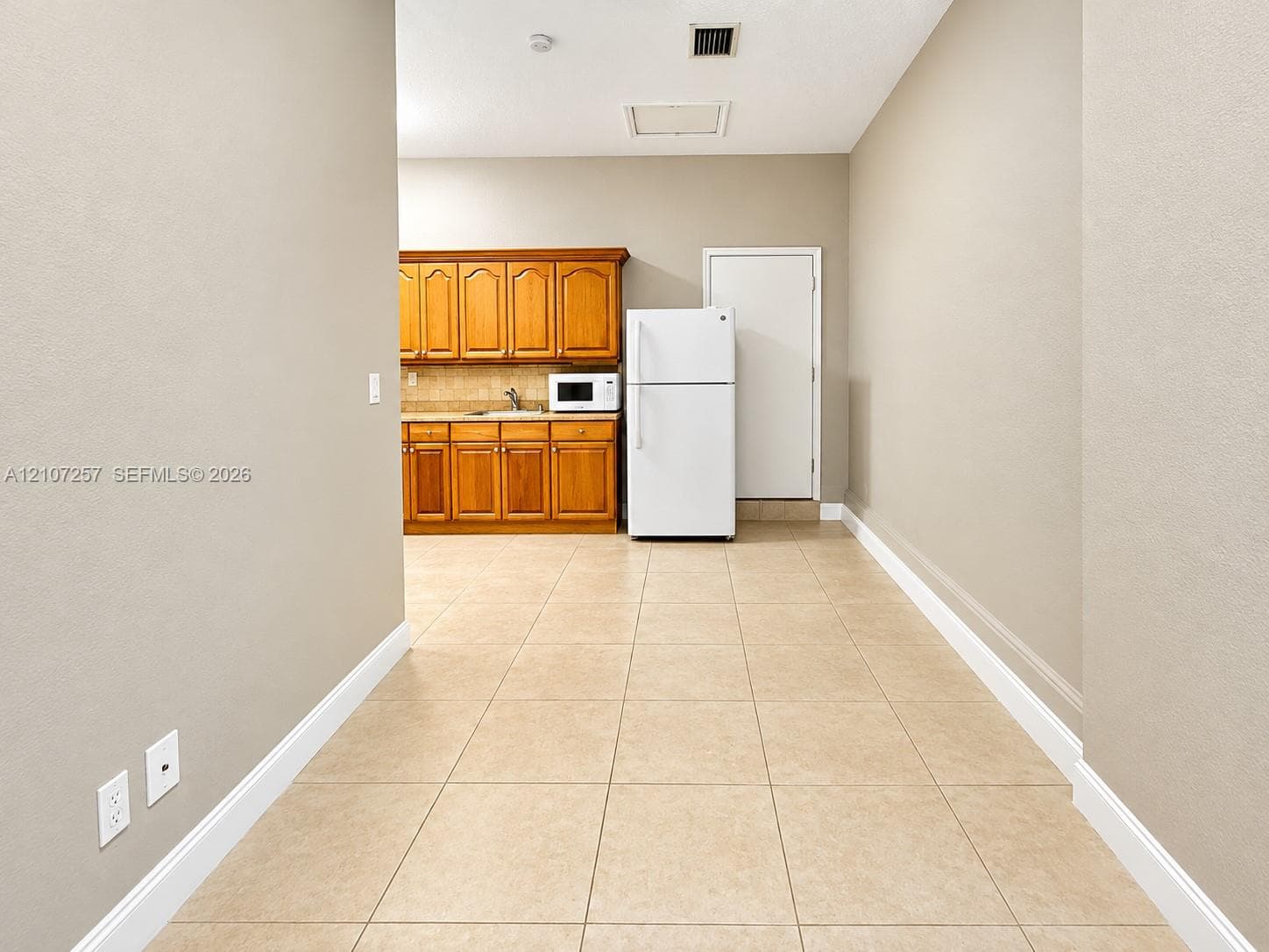 Kitchen area featuring wood cabinetry, tiled flooring, tiled backsplash, and an integrated refrigerator
