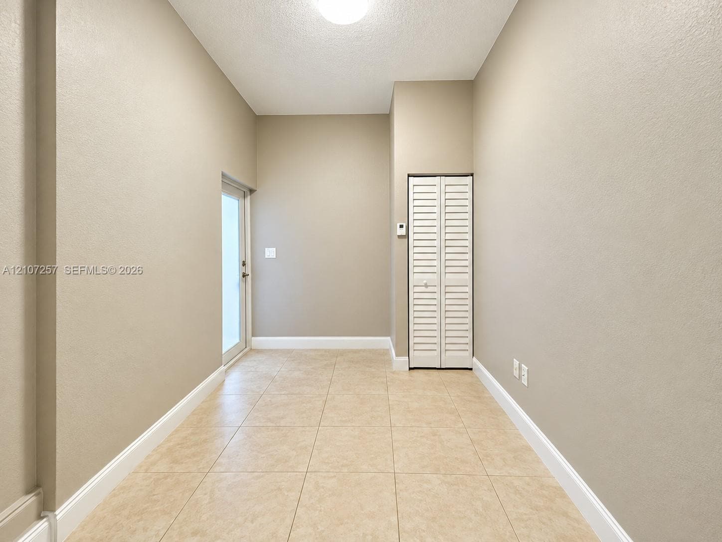 Neutral-toned interior space featuring light-colored tile flooring, a glass-paneled exterior door, and a white louvered-door closet