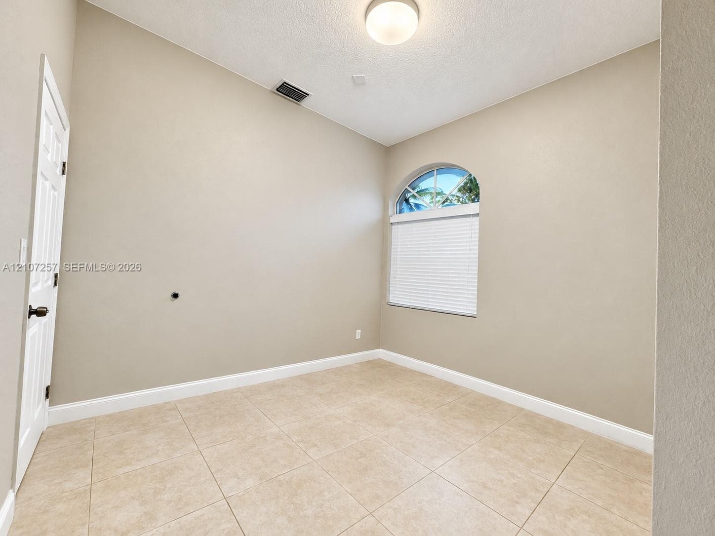 Room featuring high ceilings, arched window with decorative detailing, and ceramic tile flooring