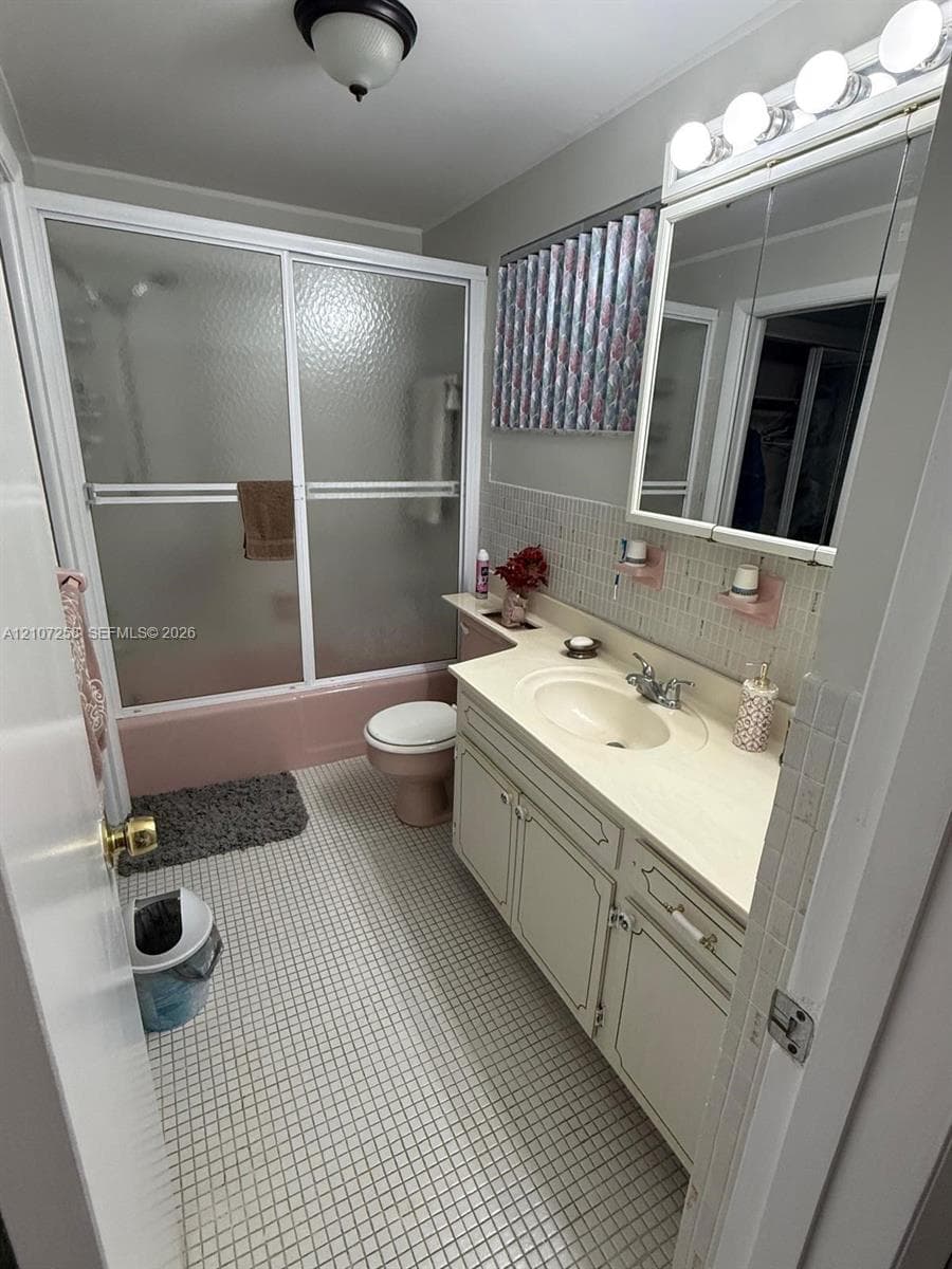 Bathroom featuring a vanity with integrated sink, glass-enclosed shower and tub combination, mirrored medicine cabinet, and tile flooring