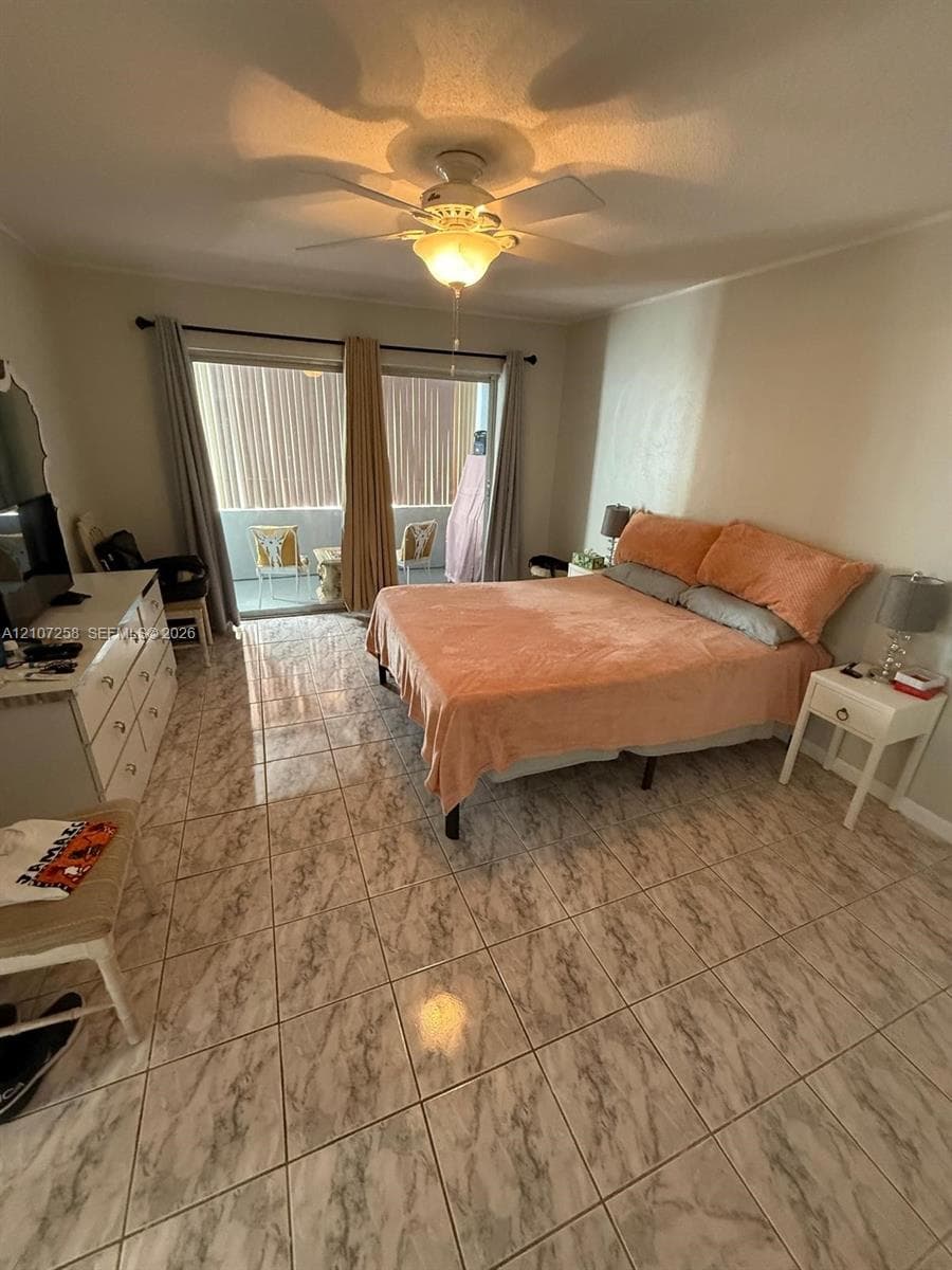 Tile flooring with neutral veining, ceiling fan with integrated lighting, and sliding glass doors providing access to a balcony