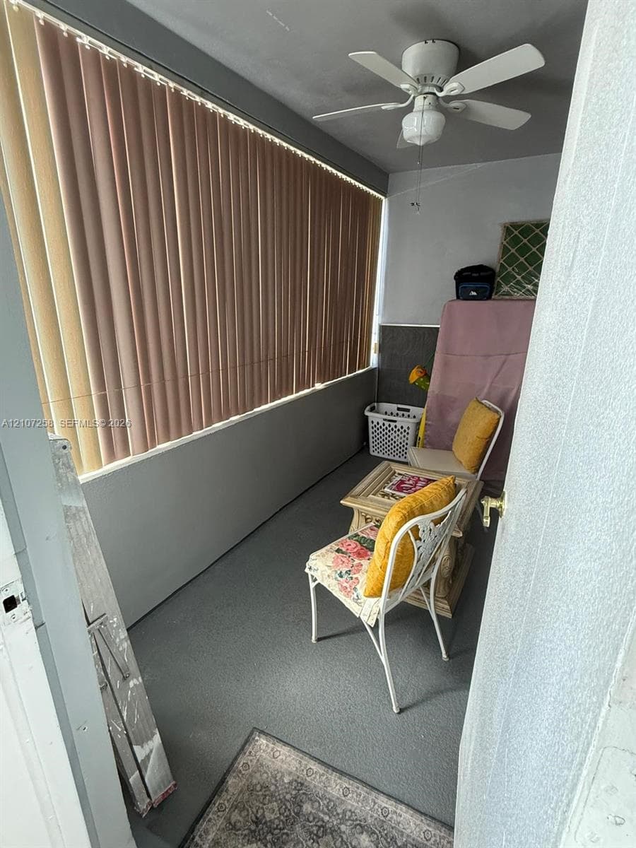 Enclosed space featuring expansive windows with vertical blinds, a ceiling-mounted fan, and solid flooring
