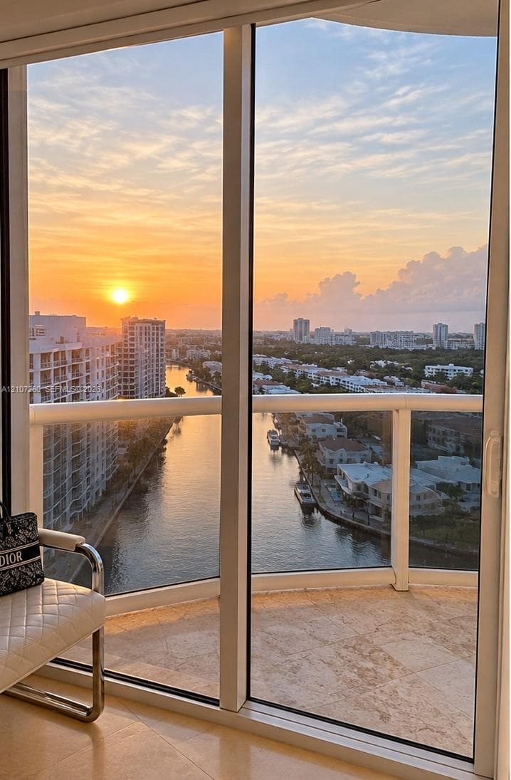 Floor-to-ceiling glass sliding doors, wrap-around balcony, stone flooring, and expansive water and skyline scenery
