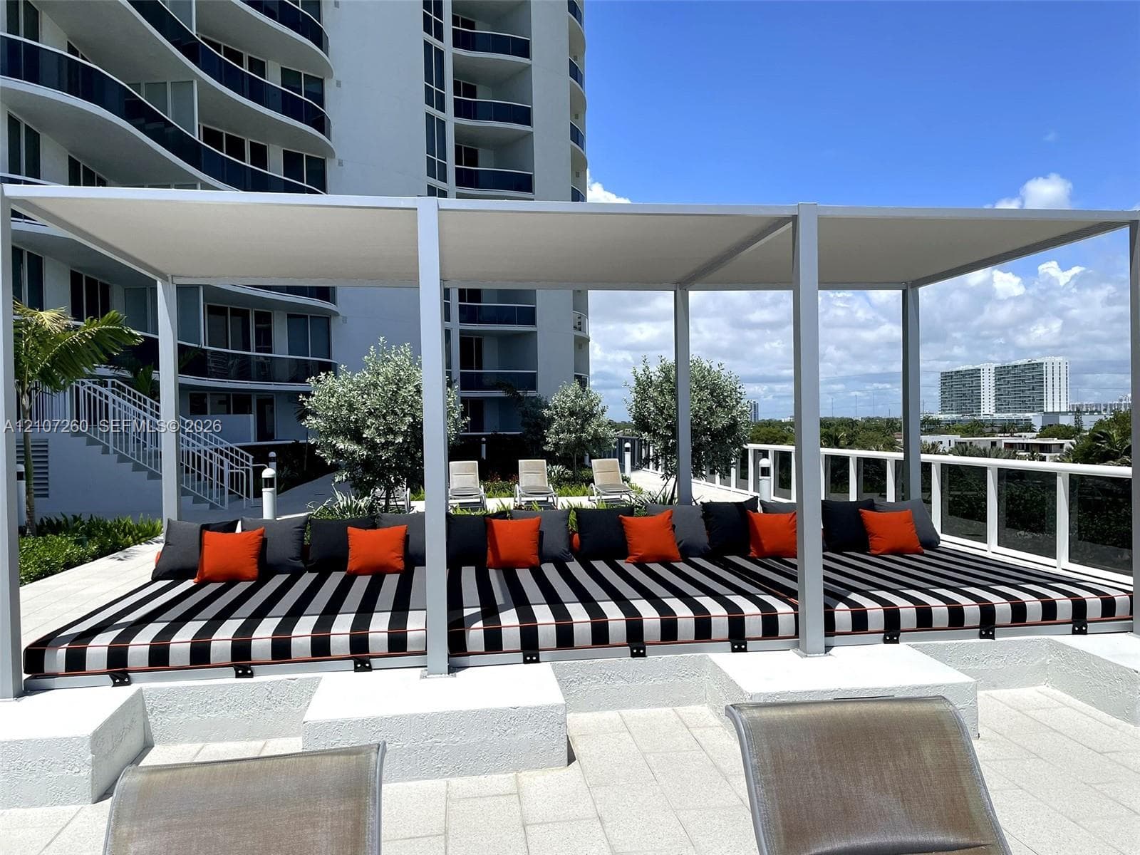 Outdoor terrace featuring a permanent, rectangular metal-framed pergola, stone-tile flooring, and a raised concrete platform