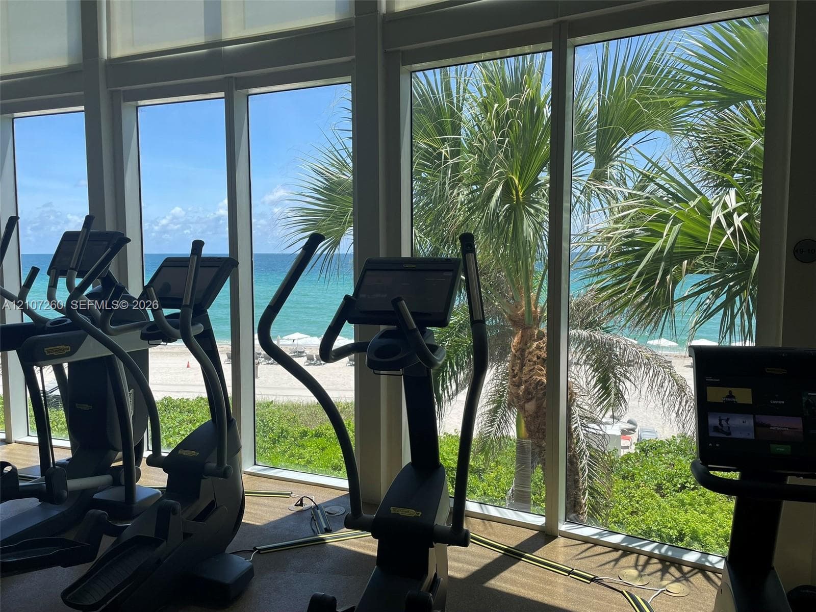 Floor-to-ceiling windows featuring ocean and beach scenery, integrated roller shades, and textured flooring