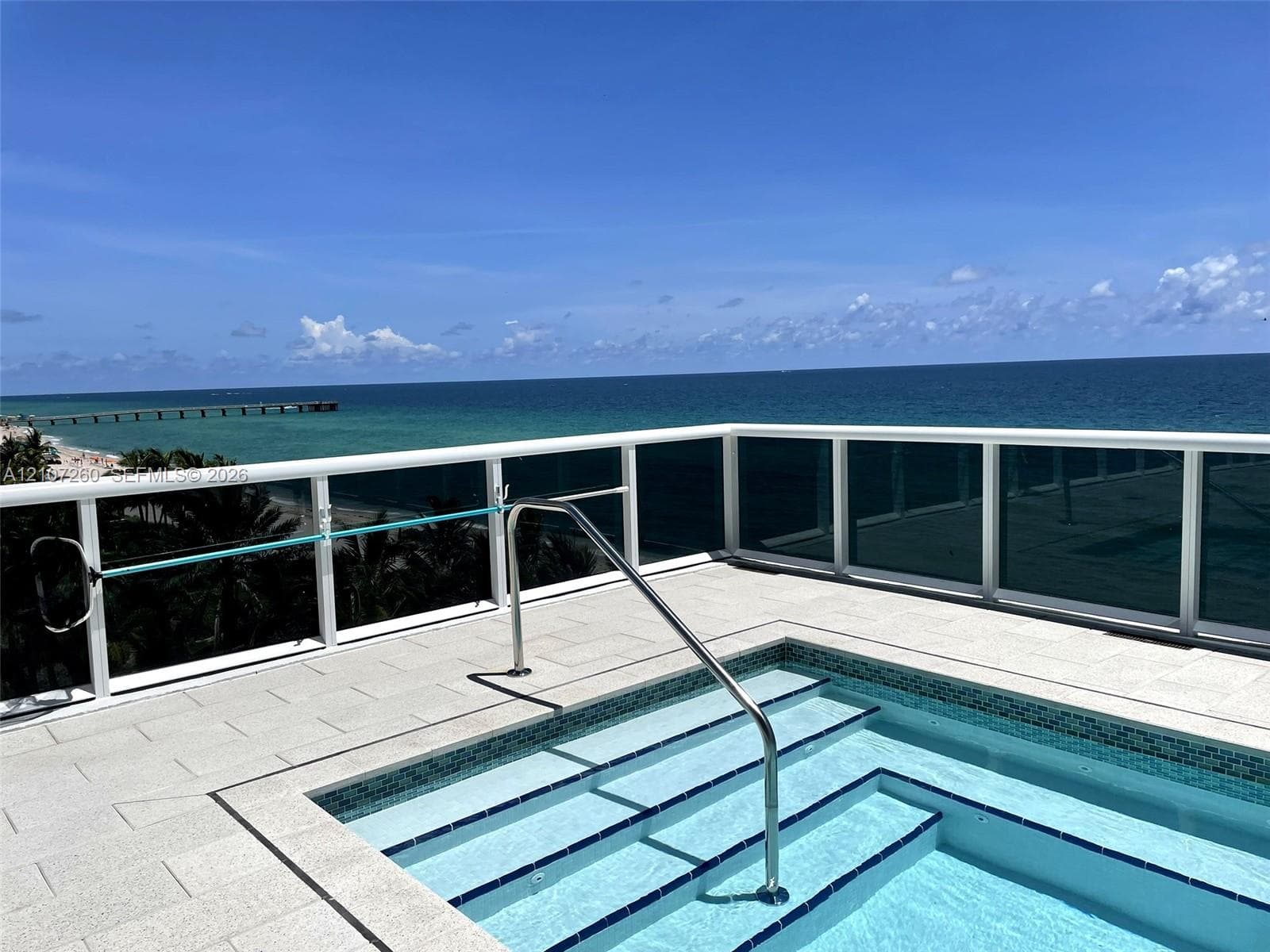 Rooftop terrace featuring a tiled deck, built-in spa with integrated steps, stainless steel handrail, and white frame glass railing