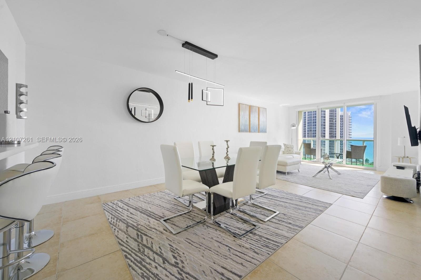 Open-concept interior featuring light-toned tile flooring, built-in breakfast bar, modern geometric pendant lighting, and floor-to-ceiling glass sliding doors