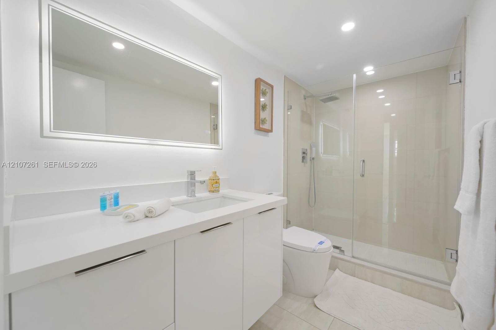 Bathroom featuring a white vanity with an integrated countertop sink, an illuminated wall-mounted mirror, a walk-in shower with a glass enclosure, and recessed lighting