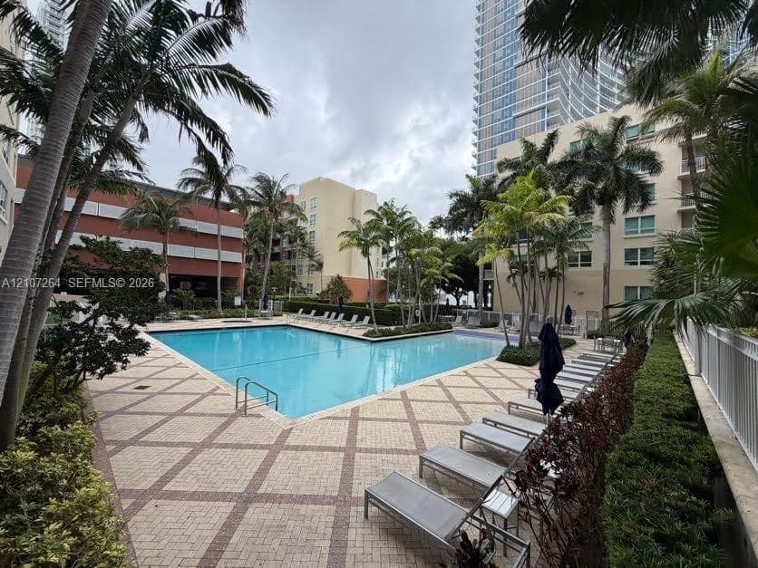 Outdoor swimming pool featuring a geometric paver deck, mature palm trees, and landscaped shrubbery