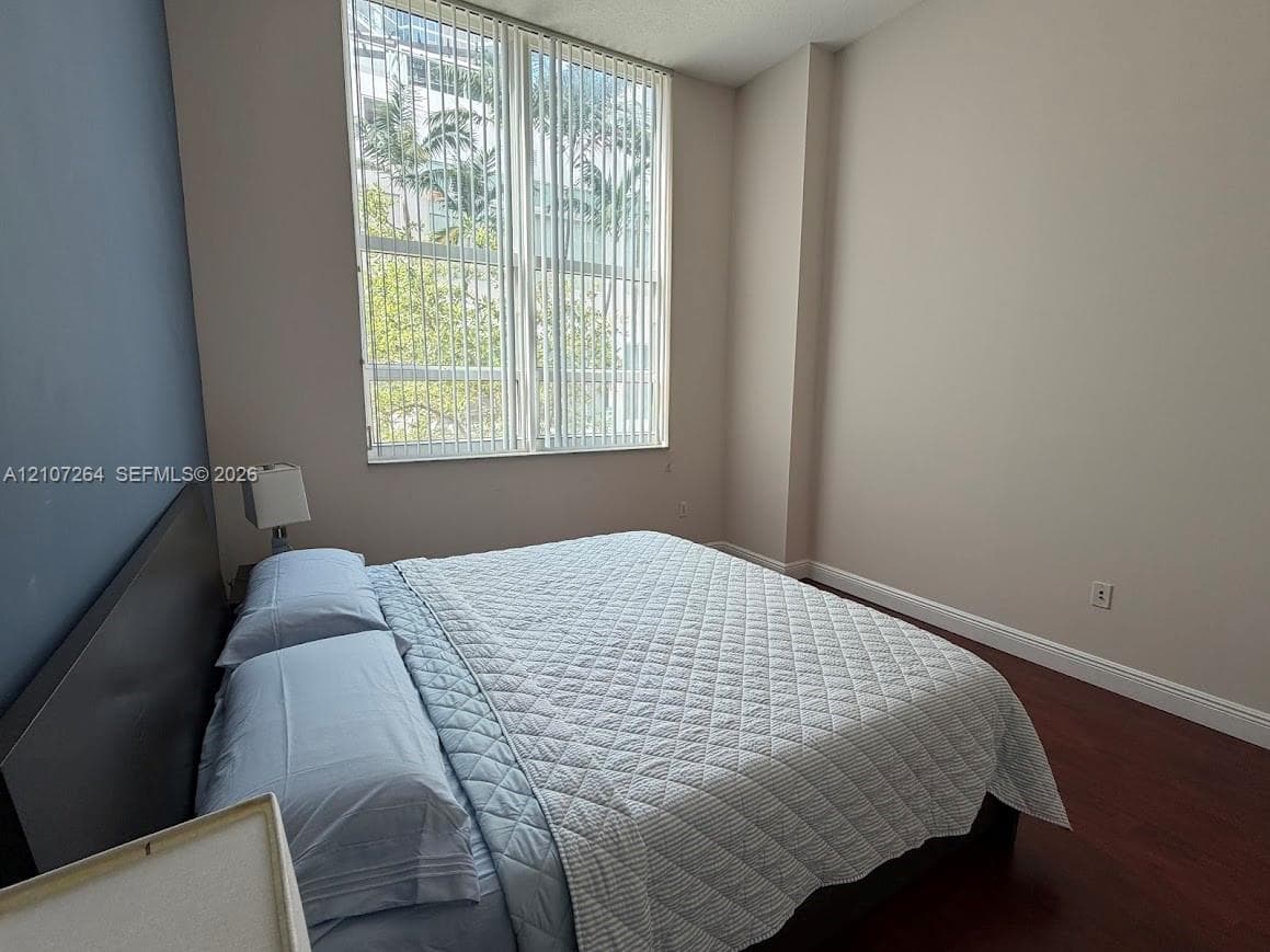 Floor-to-ceiling windows with vertical blinds, dark wood-finish flooring, and a contrast wall