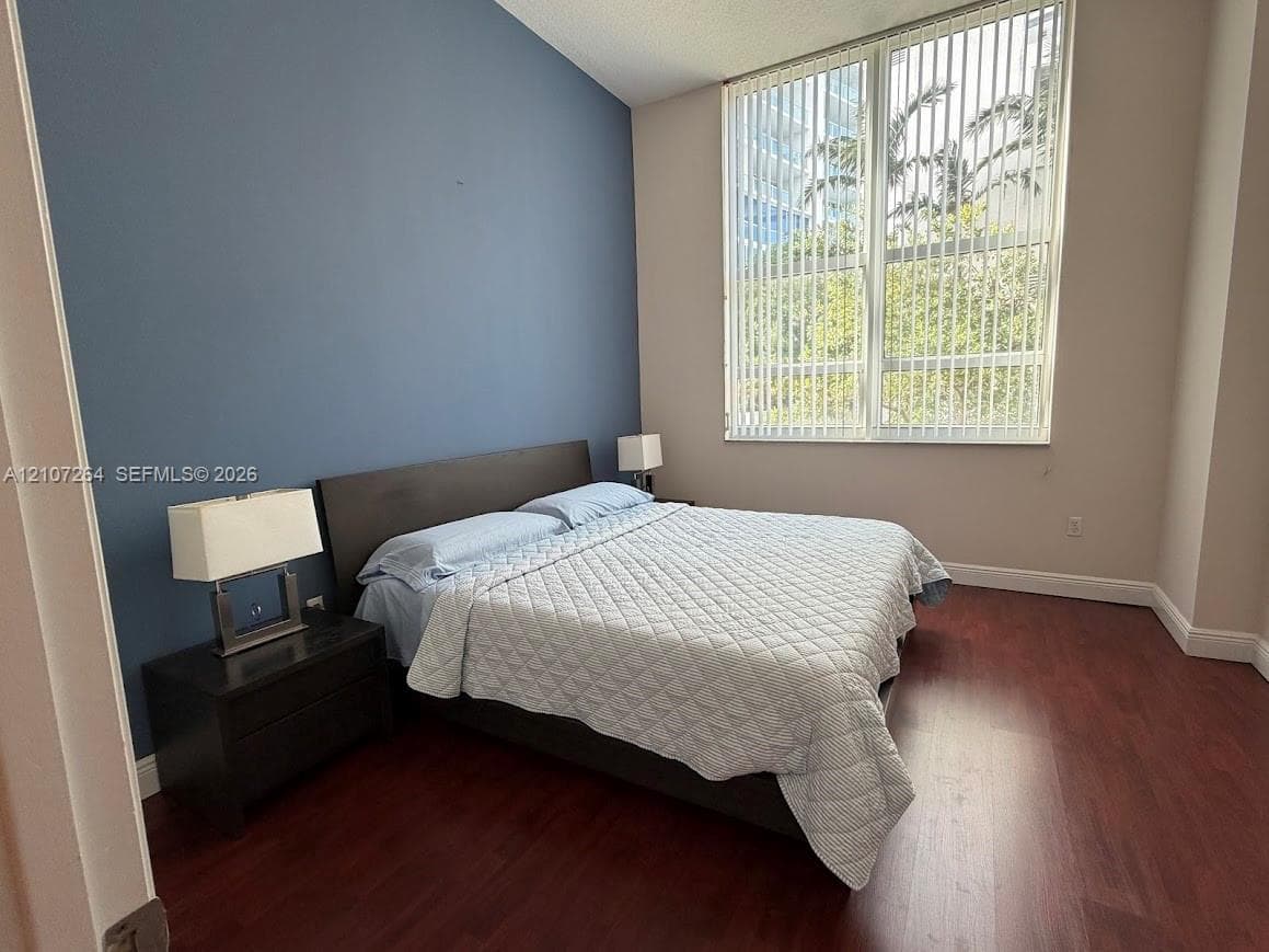High-ceiling room featuring dark wood-finish flooring, a blue accent wall, and expansive floor-to-ceiling windows with vertical blinds