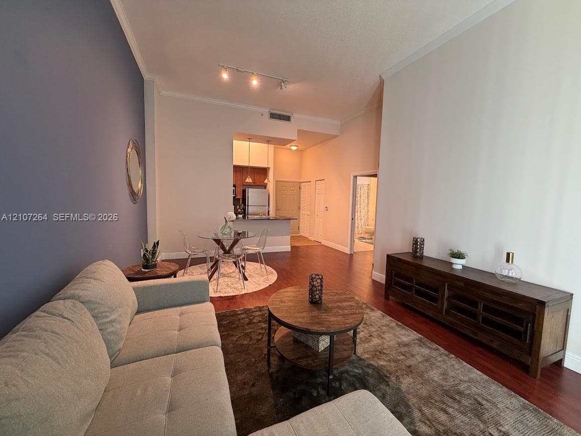 Open-concept interior featuring high ceilings, dark wood-finish flooring, a bold accent wall, and track lighting