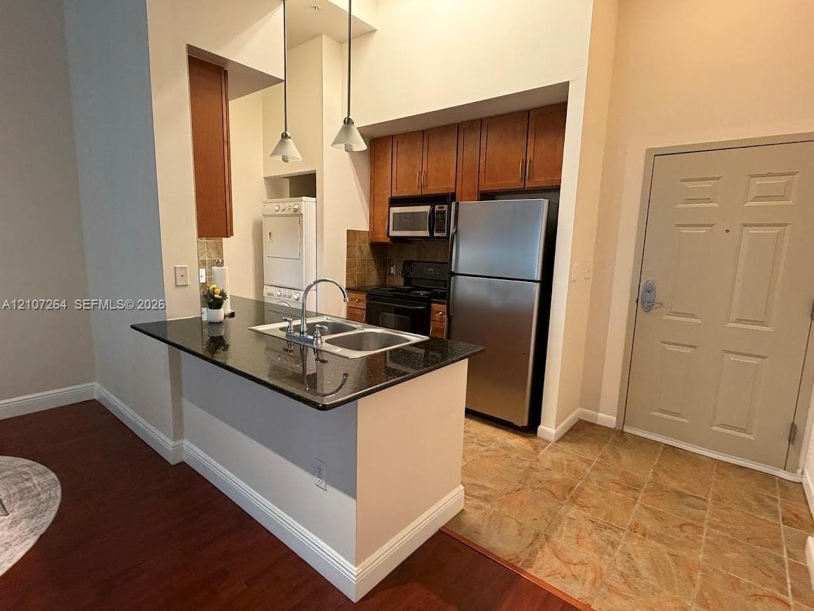 Kitchen featuring a stone-surface breakfast bar, wood-finish cabinetry, stainless steel appliances, double-basin sink with arched faucet, and recessed pendant lighting