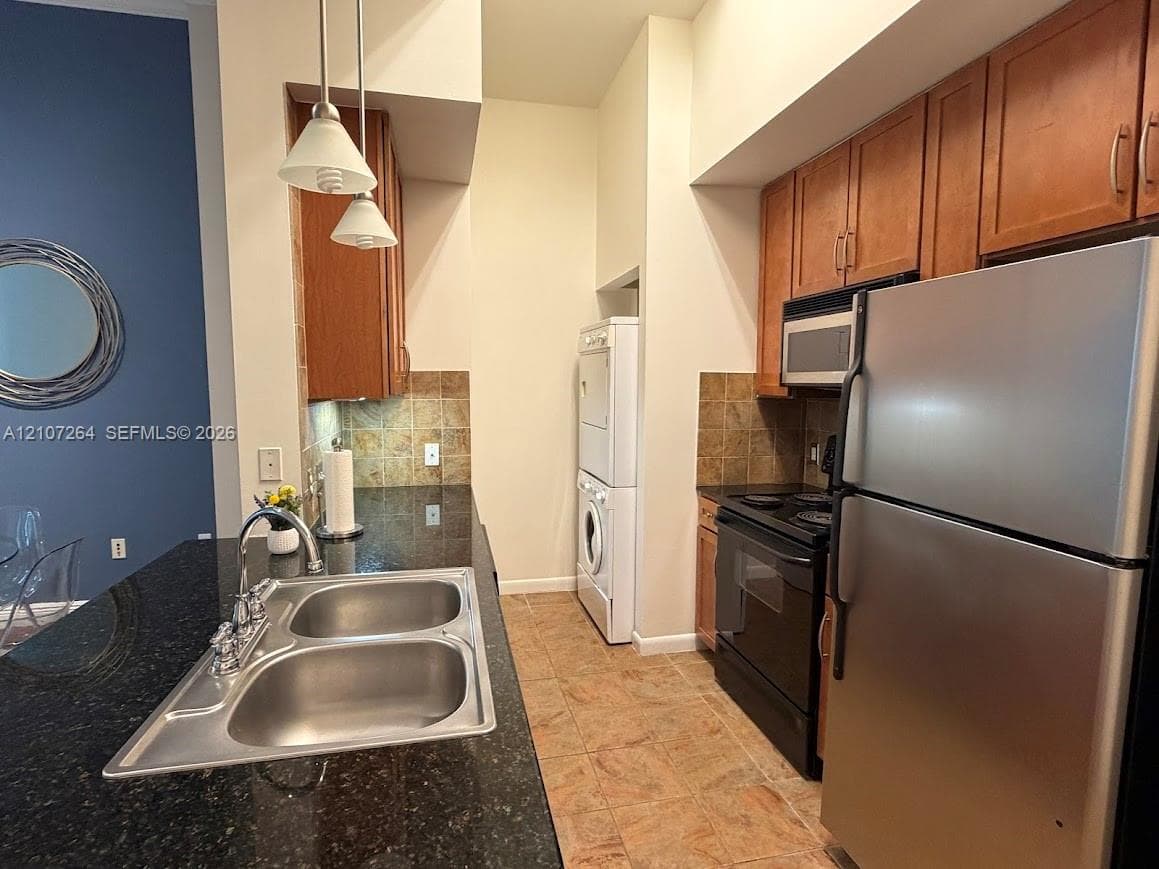 Kitchen featuring dark stone countertops, natural wood cabinetry, stainless steel appliances, tiled backsplash, and dual-basin sink with pull-down faucet