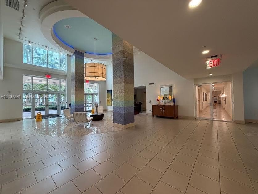 Lobby featuring tile flooring, a recessed ceiling with cove lighting, expansive floor-to-ceiling windows, and decorative mosaic-tiled columns