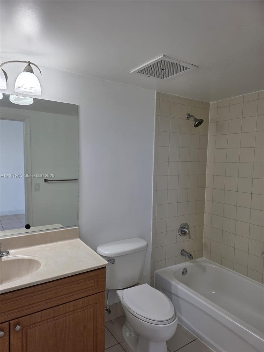Bathroom featuring a wood-finish vanity with a molded integrated sink, tiled tub surround, wall-mounted mirror, and multi-bulb light fixture