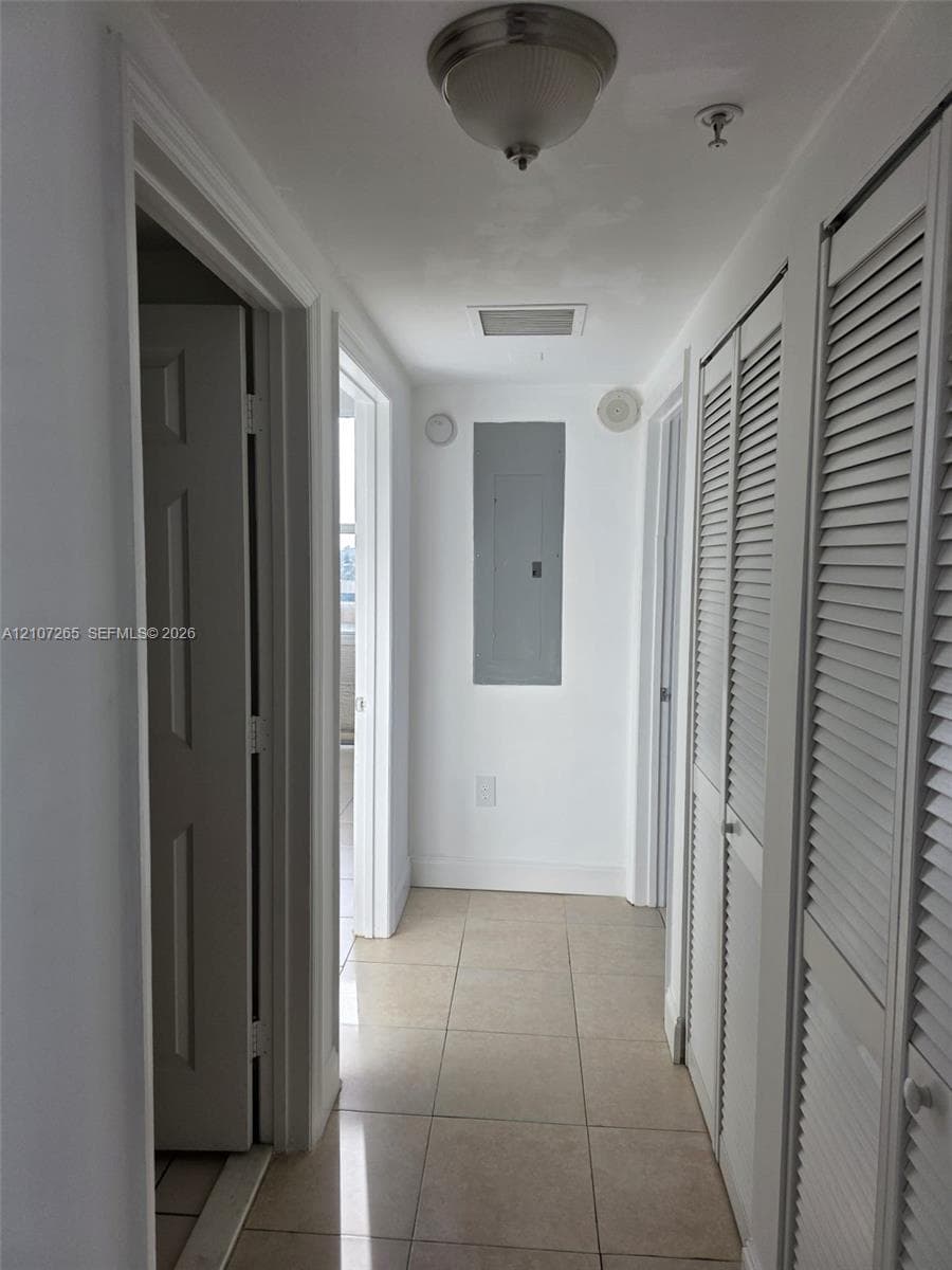 Hallway featuring light-toned tile flooring, dual louvered-style closet doors, and a neutral palette