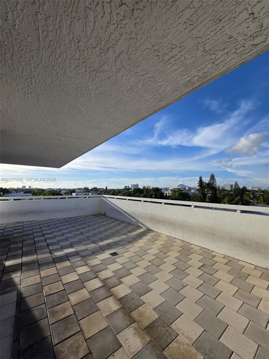 Covered outdoor terrace featuring stone paver flooring and a white masonry railing