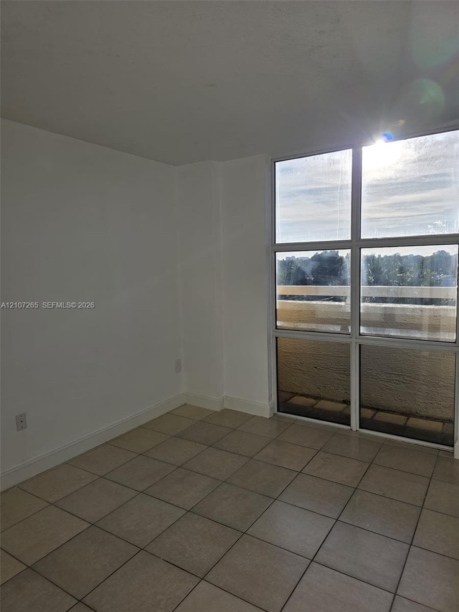 Floor-to-ceiling windows with grid detailing, ceramic tile flooring, and exterior balcony access