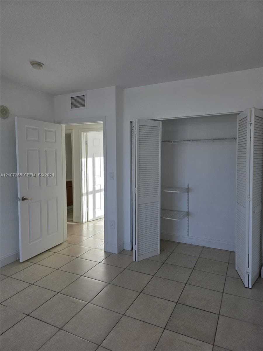 Neutral interior featuring large-format ceramic tile flooring, a walk-in closet with louvered bi-fold doors, adjustable wall-mounted shelving, and a six-panel interior door