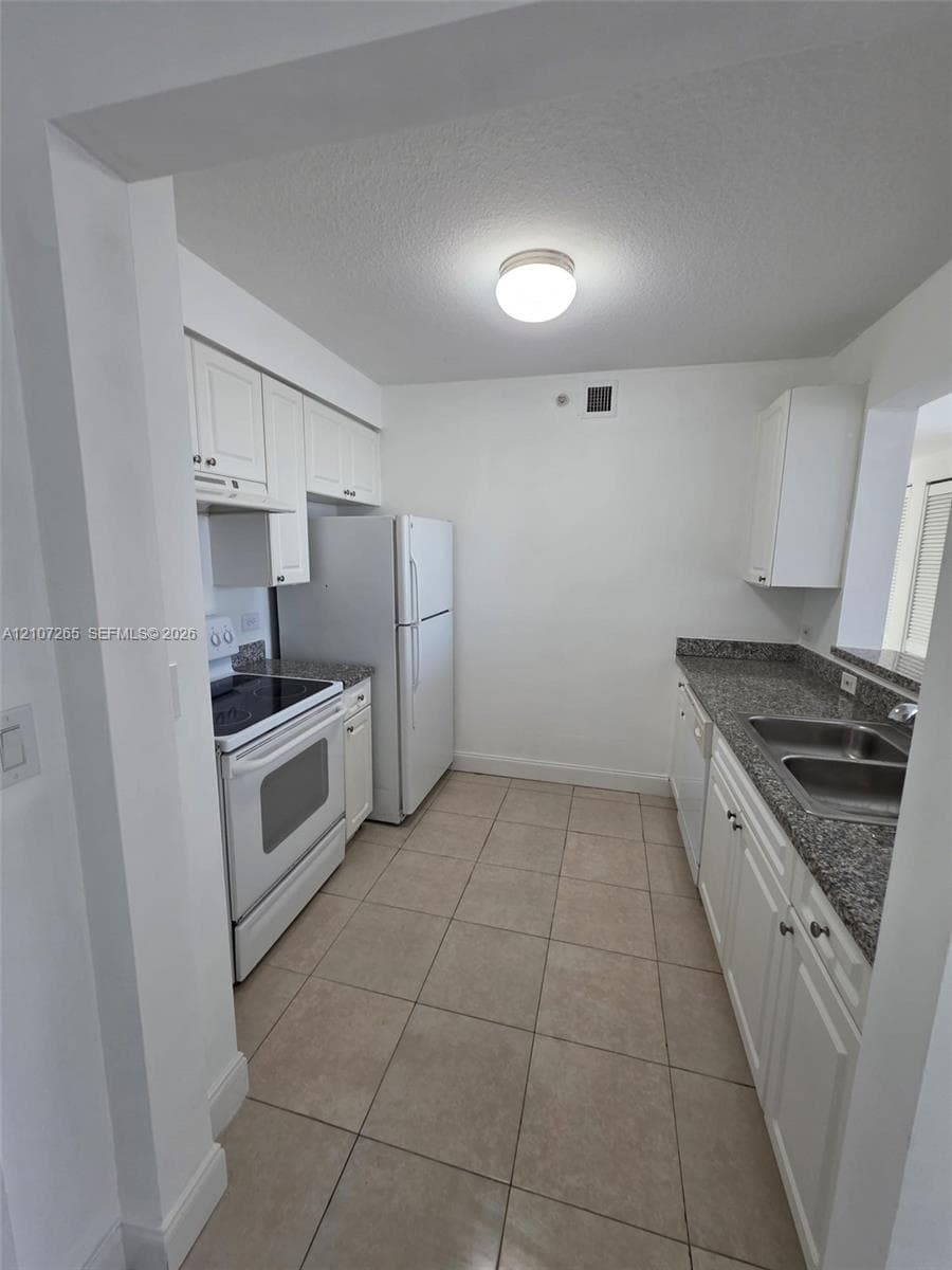 Kitchen featuring white cabinetry, stone-finish countertops, stainless steel dual-basin sink, tile flooring, and white appliance suite