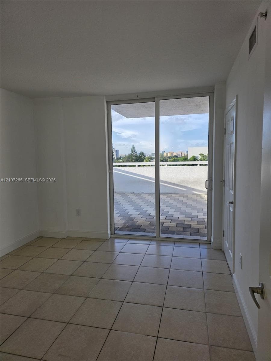 Neutral tile flooring throughout, large glass sliding door, and private outdoor balcony with patterned pavers