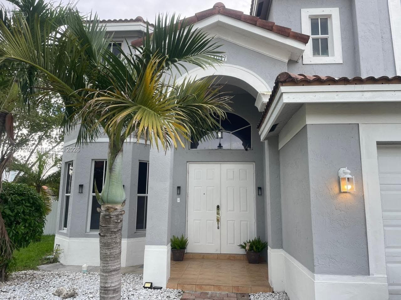 Stucco exterior featuring an arched entryway, double-door entrance, tile flooring, arched transom window, and tiled roof