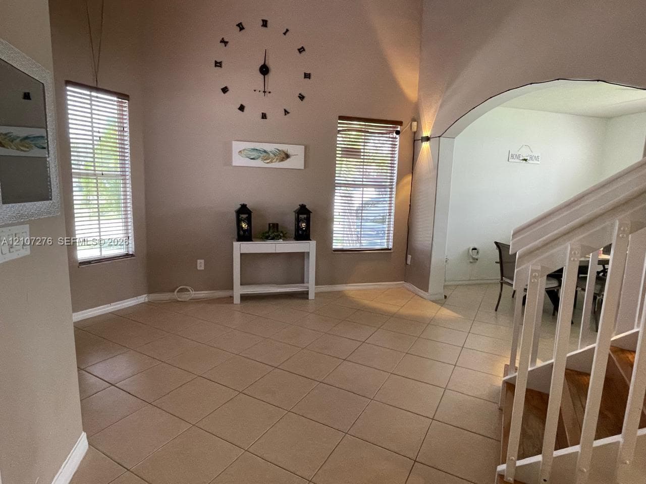 Vaulted ceilings, large-format tile flooring, dual windows with horizontal blinds, arched architectural opening, and a wooden staircase with white balusters